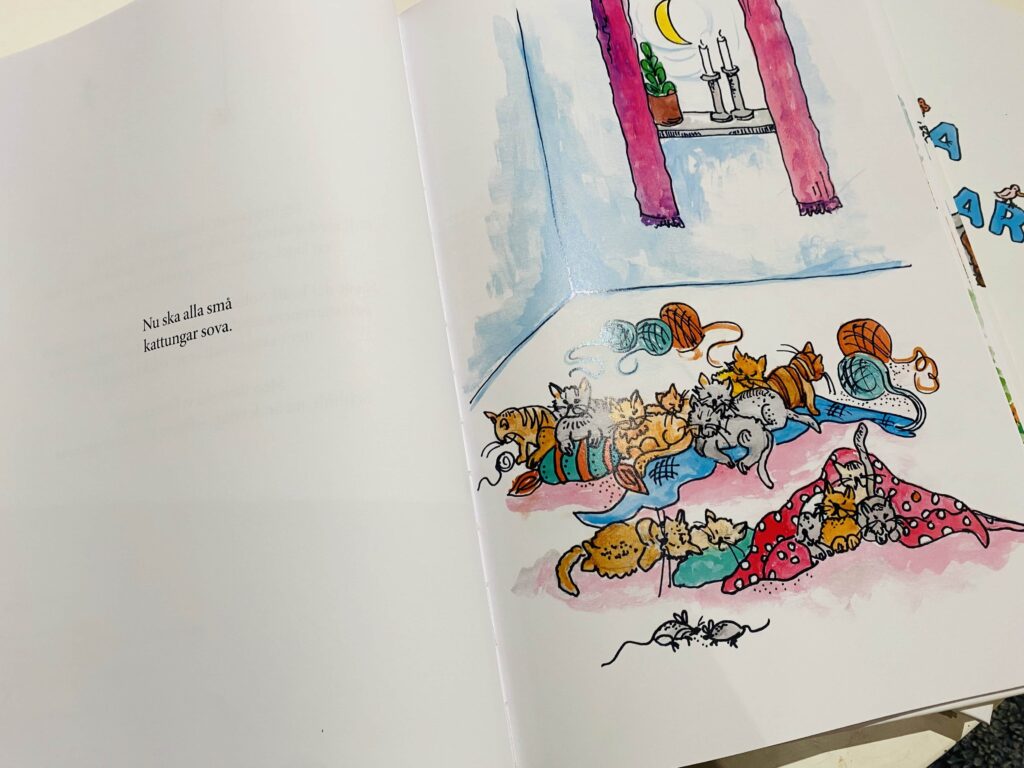 Uppslag med illustration av många katter som sover tillsammans i en mysig hemmiljö med gardiner och inredningsdetaljer. Texten lyder "Nu ska alla små kattungar sova."